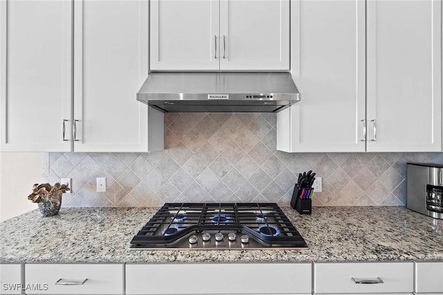 kitchen with stainless steel gas stovetop, white cabinetry, wall chimney range hood, and backsplash