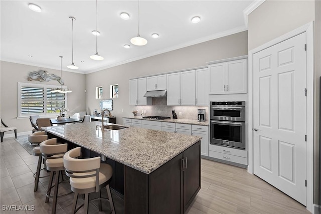 kitchen with sink, gas cooktop, an island with sink, decorative light fixtures, and white cabinets