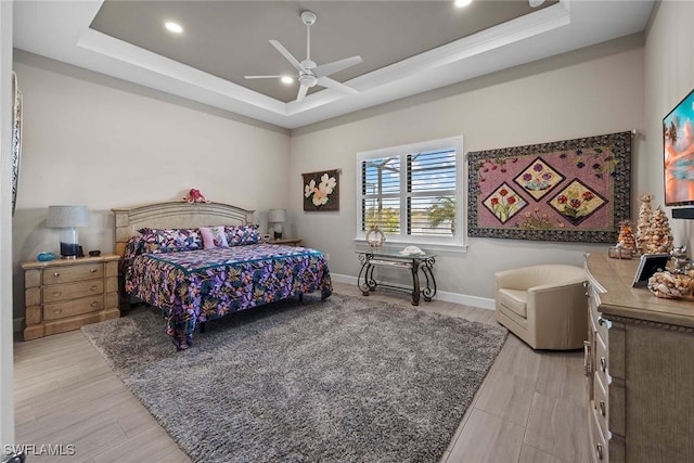 bedroom featuring ceiling fan, a raised ceiling, and light wood-type flooring