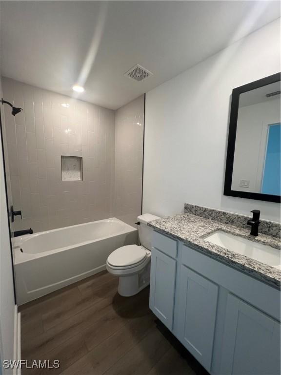 full bathroom featuring hardwood / wood-style flooring, tiled shower / bath, vanity, and toilet