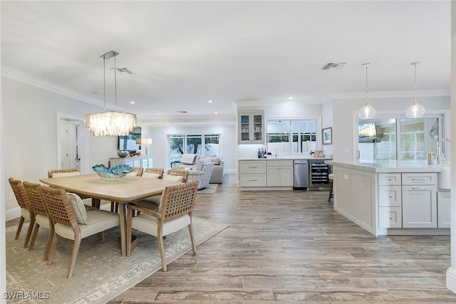 dining area featuring light hardwood / wood-style flooring, beverage cooler, crown molding, and a notable chandelier