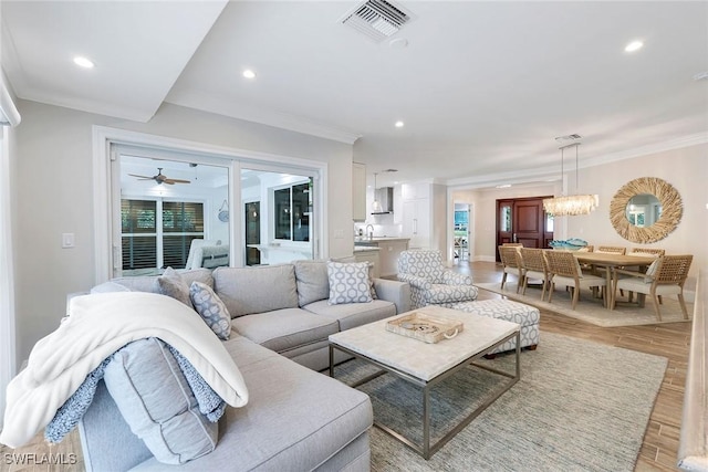 living room with ornamental molding, ceiling fan with notable chandelier, and hardwood / wood-style flooring