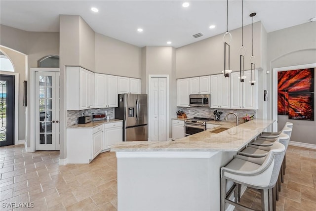 kitchen featuring kitchen peninsula, appliances with stainless steel finishes, a towering ceiling, sink, and pendant lighting