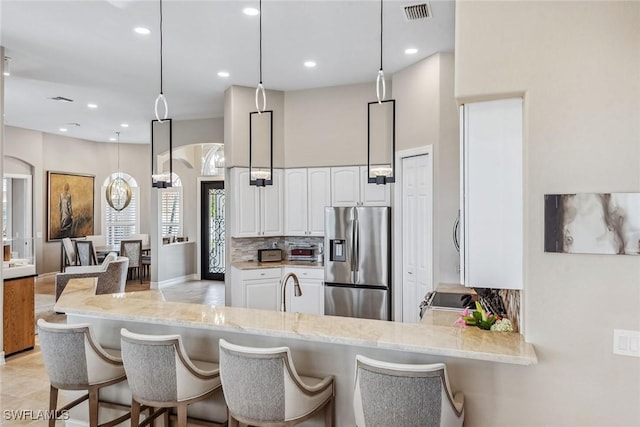 kitchen with pendant lighting, white cabinets, kitchen peninsula, tasteful backsplash, and stainless steel fridge with ice dispenser