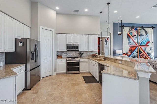 kitchen featuring kitchen peninsula, sink, appliances with stainless steel finishes, decorative light fixtures, and white cabinetry