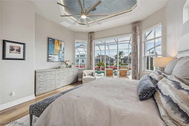 bedroom with a tray ceiling, multiple windows, ceiling fan, and hardwood / wood-style flooring