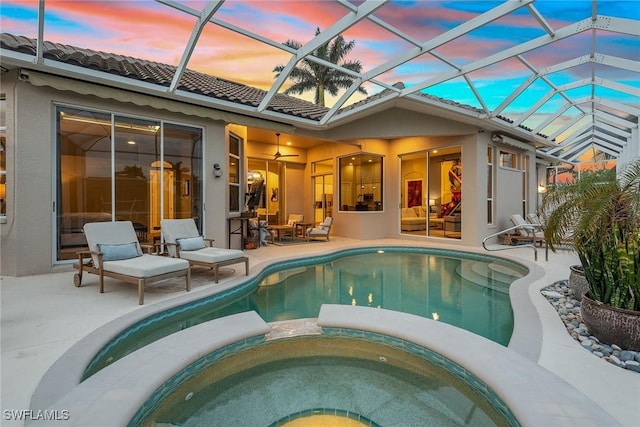 pool at dusk with an in ground hot tub, a patio area, ceiling fan, and a lanai