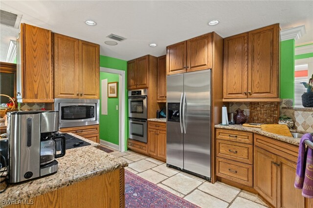 kitchen featuring built in appliances, light tile patterned flooring, light stone countertops, and backsplash