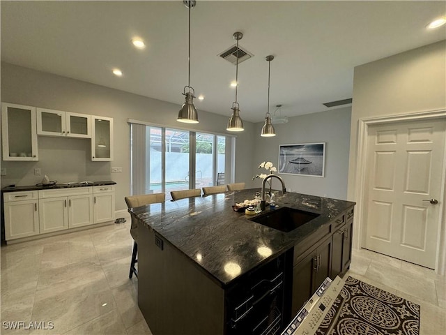 kitchen featuring dark stone countertops, white cabinetry, sink, and a kitchen island with sink