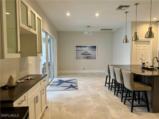 kitchen with a kitchen bar, dark stone countertops, white cabinetry, and decorative light fixtures