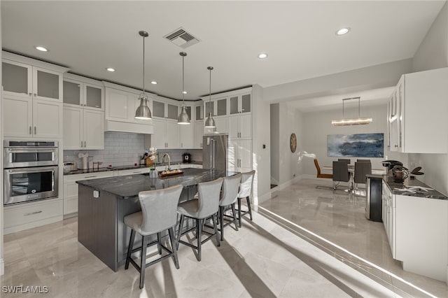 kitchen featuring stainless steel appliances, white cabinetry, dark stone countertops, and a center island with sink