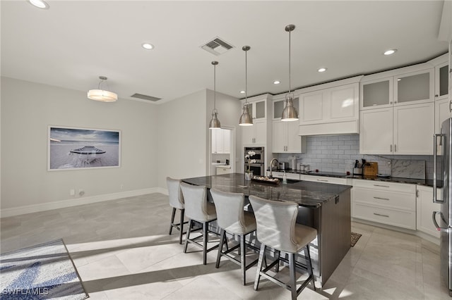 kitchen with pendant lighting, a kitchen island with sink, white cabinetry, tasteful backsplash, and a kitchen bar