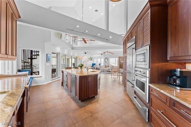 kitchen with ceiling fan, a center island, light stone counters, high vaulted ceiling, and appliances with stainless steel finishes