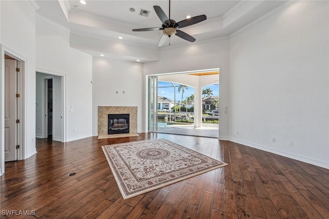 unfurnished living room with dark hardwood / wood-style flooring, a raised ceiling, ceiling fan, crown molding, and a premium fireplace