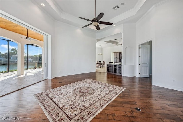 interior space with a tray ceiling, a water view, and dark hardwood / wood-style floors