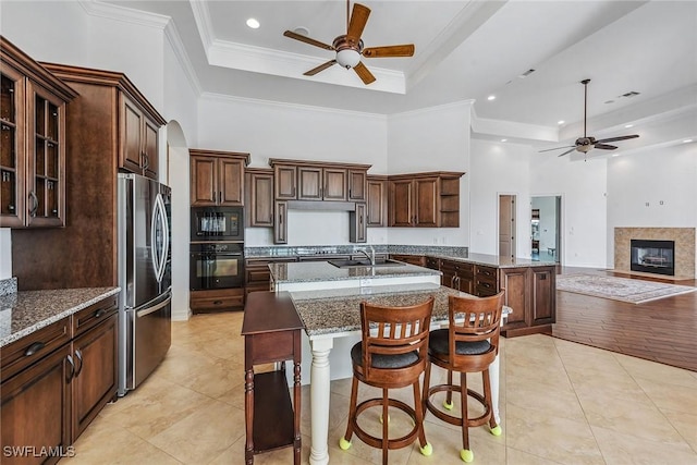 kitchen with a raised ceiling, a breakfast bar area, a kitchen island with sink, black appliances, and ornamental molding