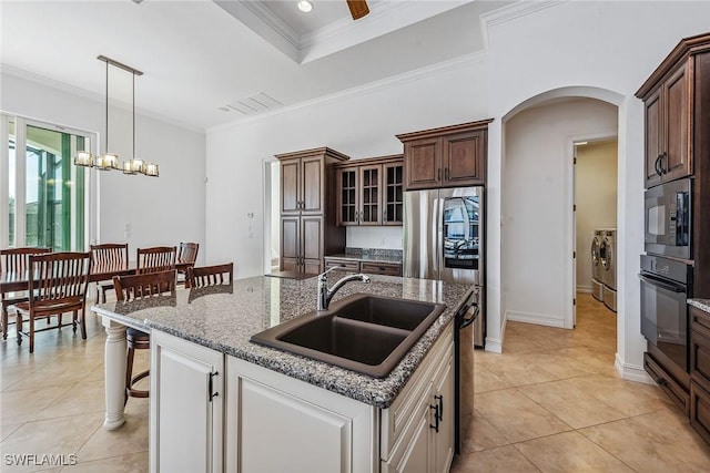 kitchen featuring a kitchen island with sink, sink, built in microwave, black oven, and a chandelier