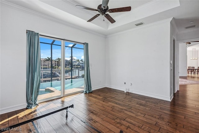 empty room featuring dark hardwood / wood-style flooring, a tray ceiling, ceiling fan, and ornamental molding