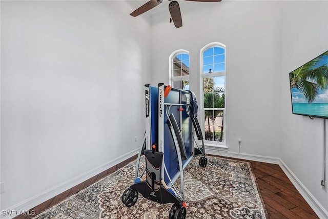 exercise room with ceiling fan, hardwood / wood-style floors, and a high ceiling