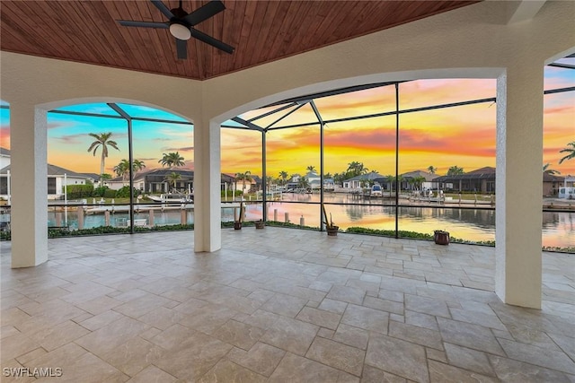 patio terrace at dusk featuring a lanai, ceiling fan, and a water view