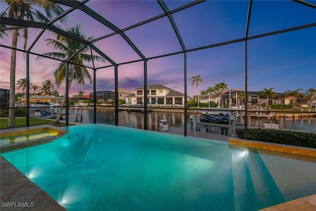 pool at dusk with an in ground hot tub, a water view, a dock, and a lanai