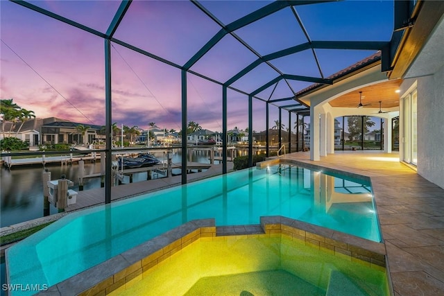 pool at dusk with a lanai, a water view, and a dock