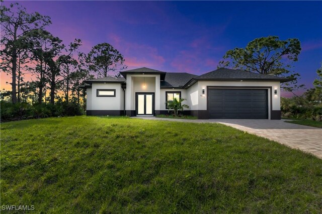 prairie-style house featuring a garage, decorative driveway, a lawn, and stucco siding