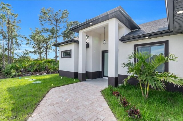 entrance to property with a yard, a shingled roof, and stucco siding