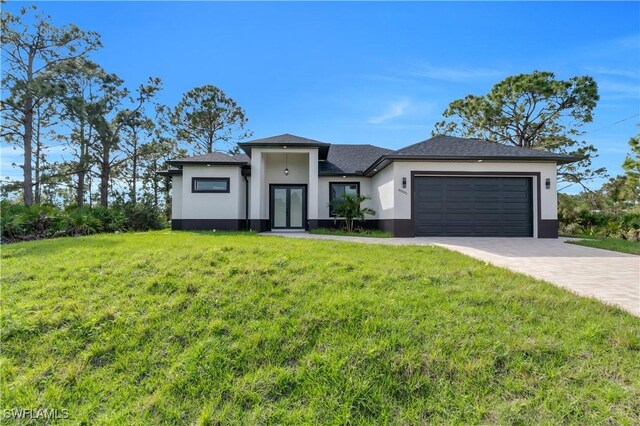 prairie-style house featuring an attached garage, stucco siding, decorative driveway, and a front yard