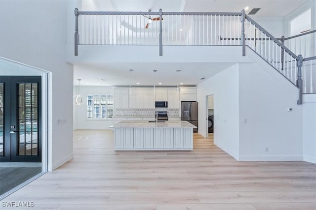 kitchen with a center island with sink, hanging light fixtures, stainless steel appliances, french doors, and white cabinetry