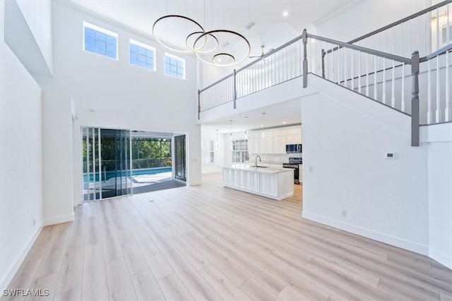 unfurnished living room featuring sink, light hardwood / wood-style flooring, and a towering ceiling