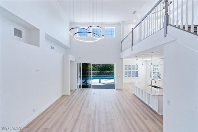 unfurnished living room with sink, a high ceiling, and light wood-type flooring