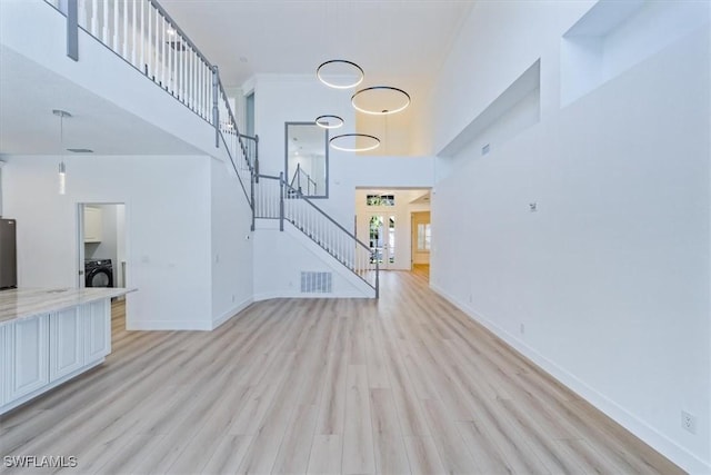 unfurnished living room featuring a high ceiling, light hardwood / wood-style flooring, and washer / clothes dryer