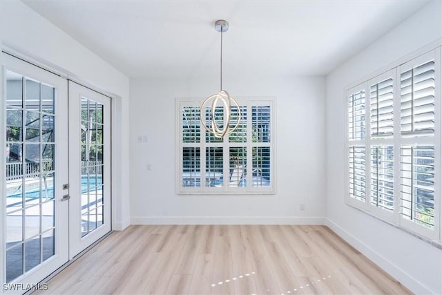 unfurnished dining area featuring a notable chandelier, french doors, light hardwood / wood-style floors, and plenty of natural light