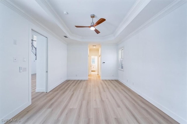 unfurnished room featuring light hardwood / wood-style floors, ceiling fan, a tray ceiling, and ornamental molding