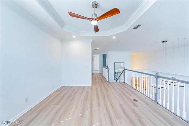 spare room with a raised ceiling, ceiling fan, light hardwood / wood-style floors, and crown molding