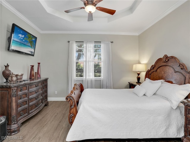 bedroom with ornamental molding, light wood-type flooring, ceiling fan, and a tray ceiling