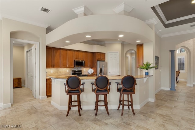 kitchen featuring a kitchen bar, ornamental molding, light stone counters, kitchen peninsula, and stainless steel appliances