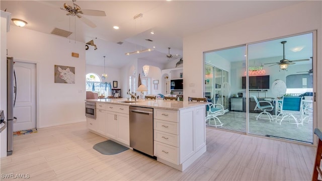 kitchen with appliances with stainless steel finishes, vaulted ceiling, white cabinets, light stone counters, and sink