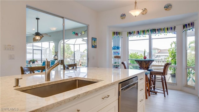 kitchen featuring white cabinetry, ceiling fan, dishwasher, hanging light fixtures, and light stone counters