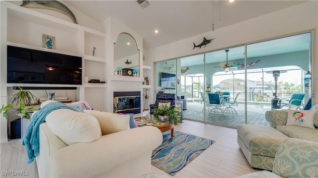 living room with ceiling fan, built in shelves, and vaulted ceiling