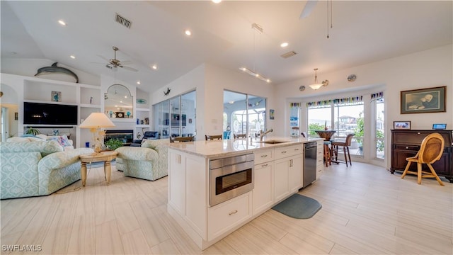 kitchen featuring decorative light fixtures, white cabinetry, built in shelves, a kitchen island with sink, and built in microwave