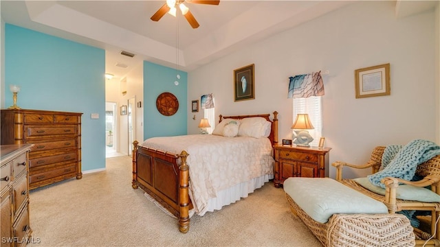 bedroom with ceiling fan, ensuite bathroom, light carpet, and a raised ceiling