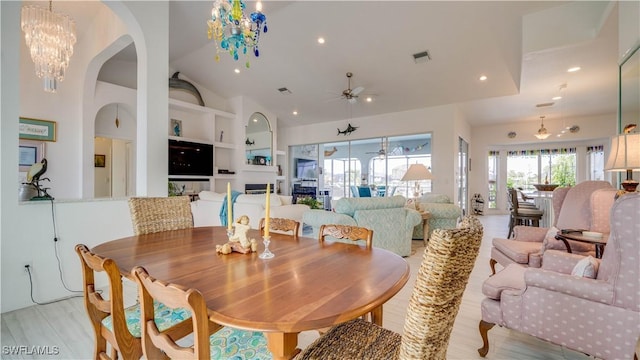 dining space with built in shelves, ceiling fan with notable chandelier, and light hardwood / wood-style floors