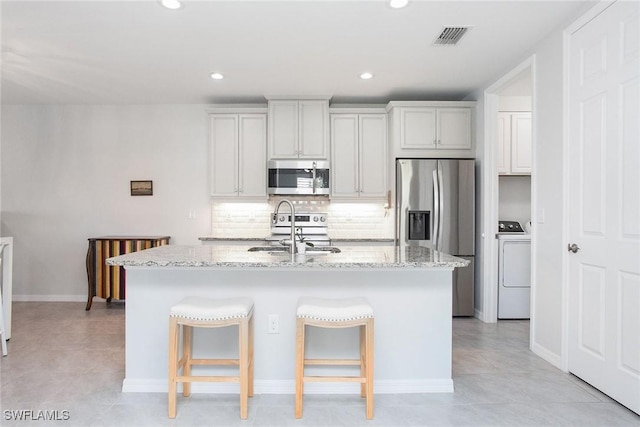 kitchen featuring visible vents, appliances with stainless steel finishes, a sink, an island with sink, and washer / dryer