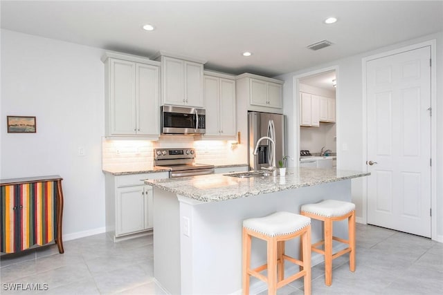 kitchen with light stone counters, visible vents, decorative backsplash, appliances with stainless steel finishes, and a kitchen breakfast bar