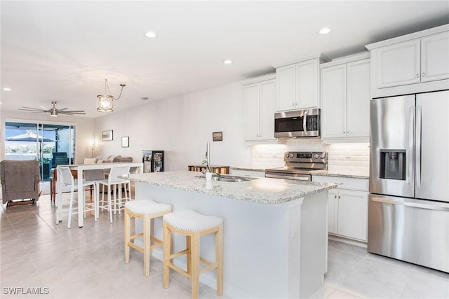 kitchen with ceiling fan, a sink, open floor plan, appliances with stainless steel finishes, and decorative backsplash