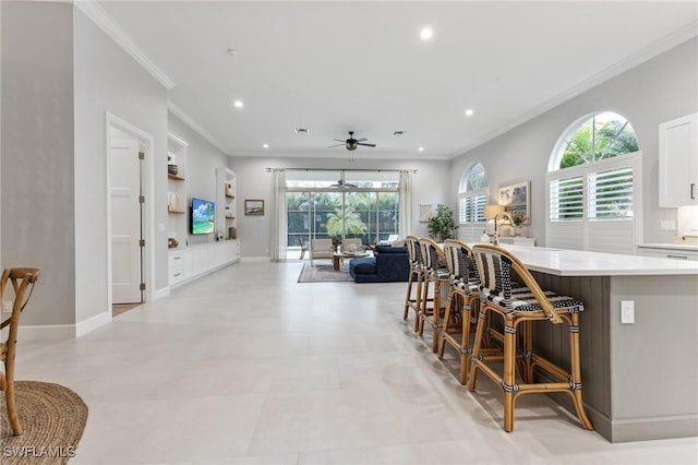 kitchen with ornamental molding, ceiling fan, a healthy amount of sunlight, white cabinetry, and a breakfast bar area