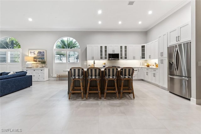 kitchen with white cabinets, ornamental molding, appliances with stainless steel finishes, a kitchen island, and a breakfast bar area