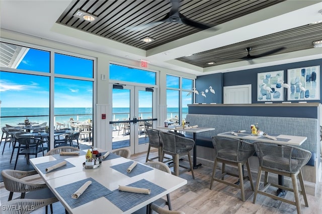 dining space with hardwood / wood-style floors, french doors, a raised ceiling, a water view, and ceiling fan